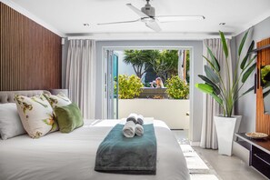 Un dormitorio moderno con cama, ventilador de techo y vistas a un balcón con plantas.