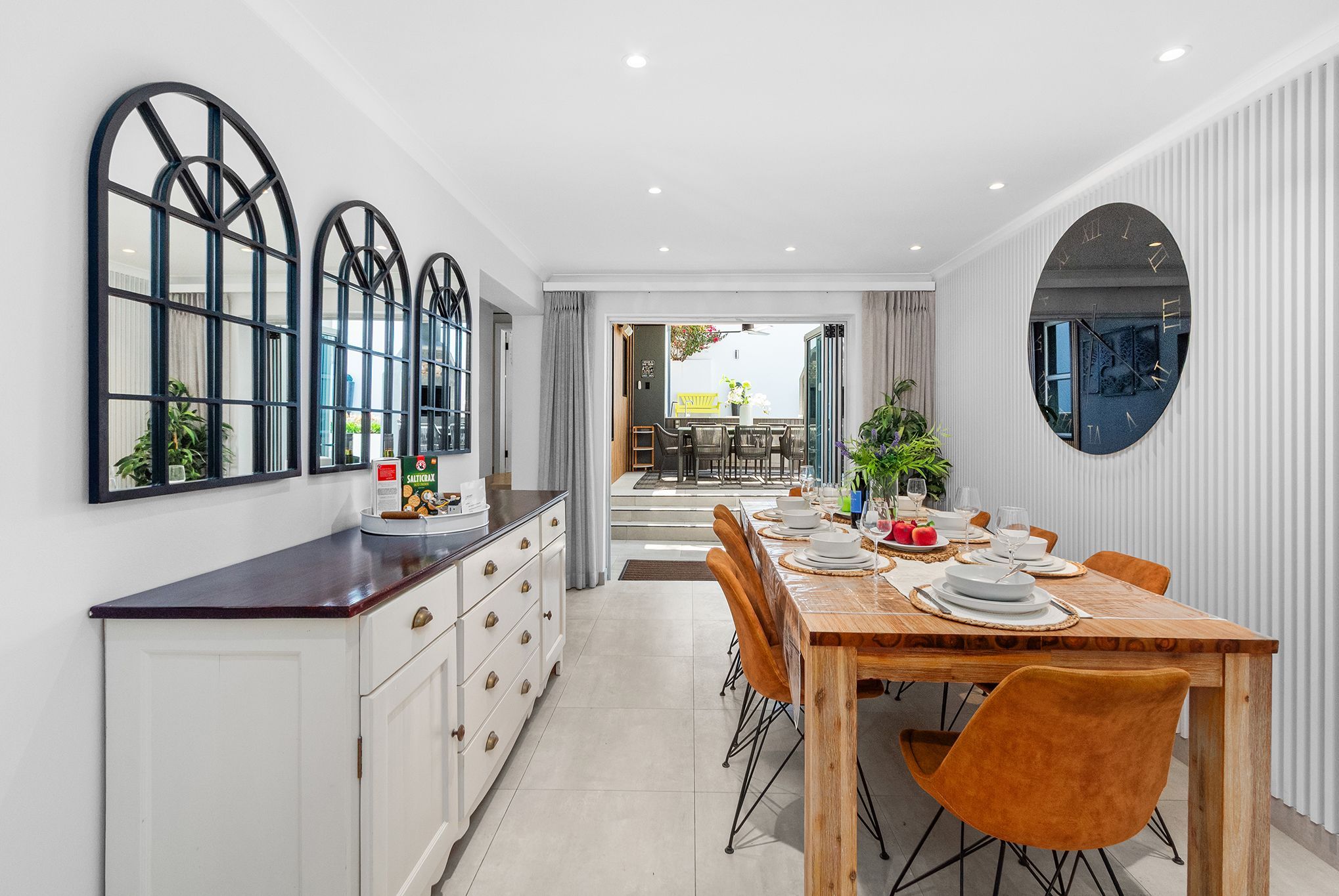 A modern dining area with a wooden table set for four, white cabinets, and a large mirror on the wall.