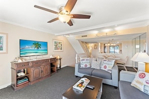 A living room with a television, a coffee table, a sofa, and a ceiling fan.