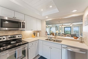 A modern kitchen with stainless steel appliances, white cabinetry, and a large window offering a view of the outdoors.