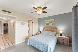 A bedroom with a bed, nightstands, a ceiling fan, a painting, and a hallway.