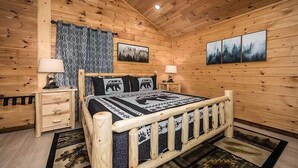 Dormitorio de cabaña de madera con cama, dos mesitas de noche y un cuadro colgado en la pared.