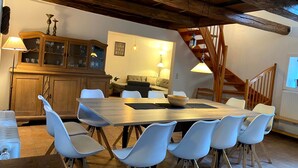 Un coin repas avec une table en bois et des chaises blanches, un buffet en bois doté de portes en verre, et un escalier avec des rampes en bois.