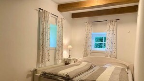 Une chambre à coucher avec un lit, des rideaux, une fenêtre et une table de chevet avec une lampe.