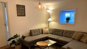 Un salon moderne avec un canapé d’angle, une table basse en verre, un lampadaire et une estampe botanique encadrée accrochée au mur.
