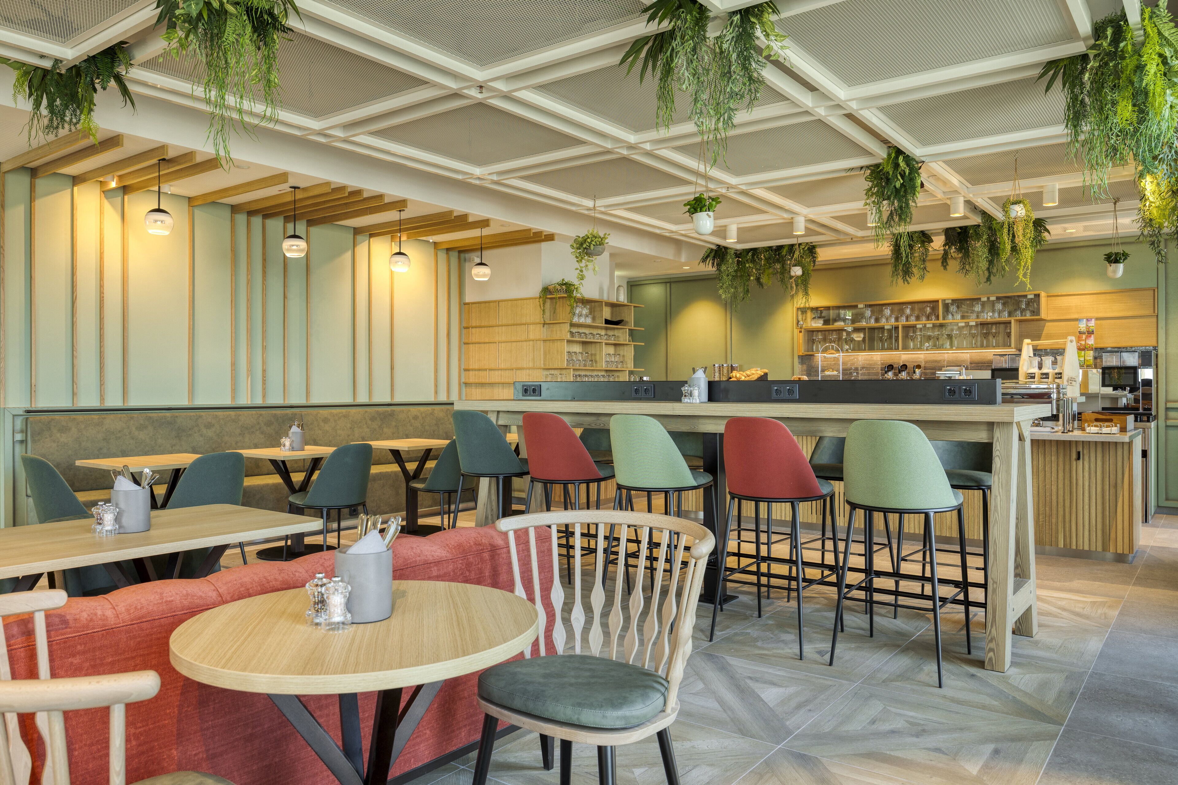 A modern restaurant with wooden tables and chairs, a bar area, and hanging plants.