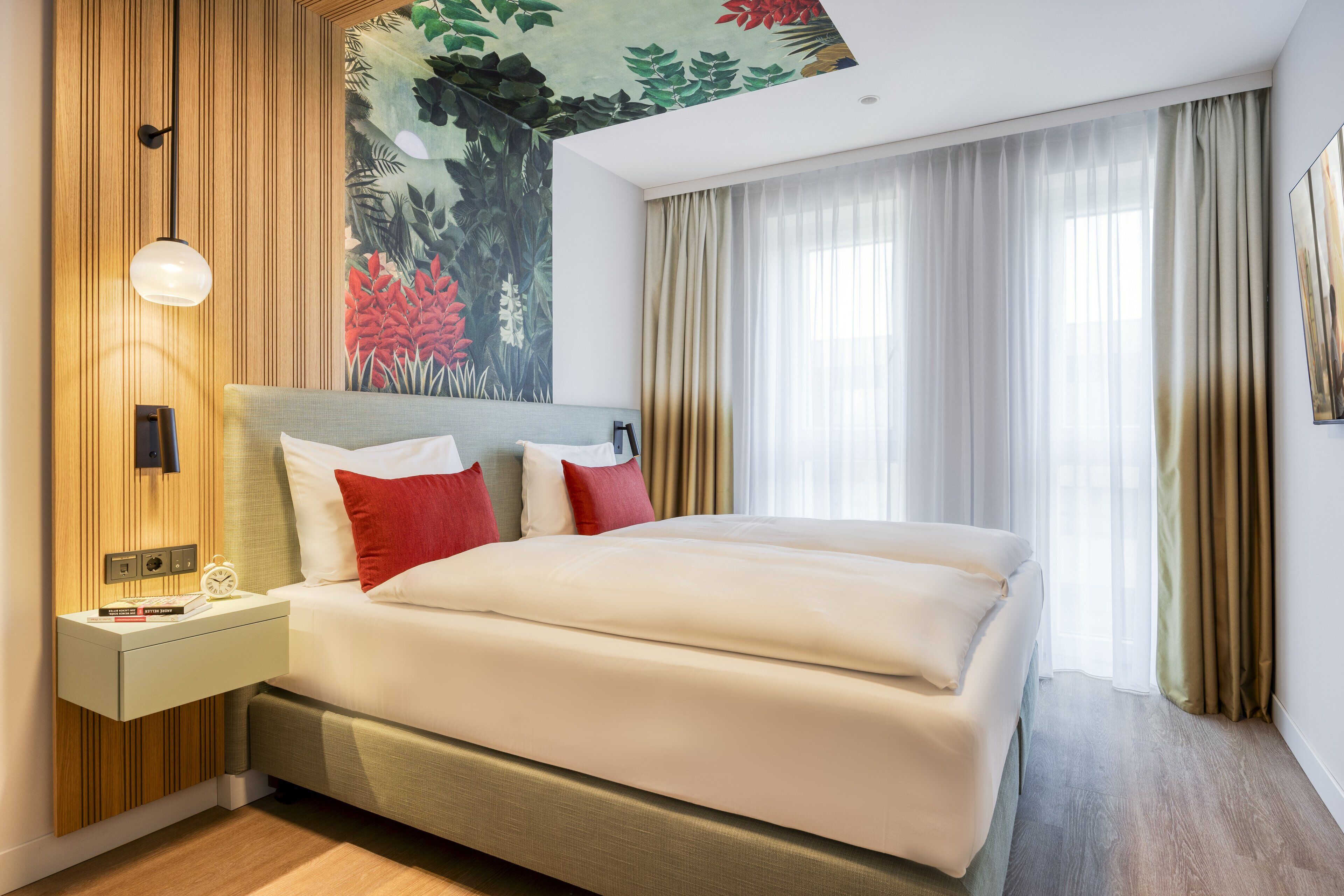 Habitación de hotel con cama, mesita de noche, lámpara de pared, un cuadro y ventana con cortinas.