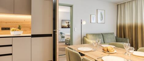 Une cuisine moderne avec un plan de travail en bois, un coin repas avec une table dressée pour quatre personnes, et un salon avec un canapé et un tableau accroché au mur.