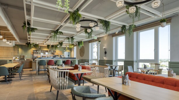 Un restaurant moderne avec de hauts plafonds, des plantes suspendues et de grandes fenêtres.