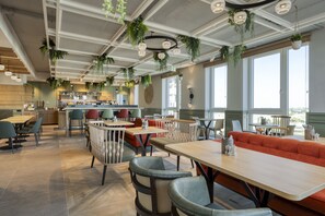 A modern restaurant with high ceilings, hanging plants, and large windows. - Citadines Danube Vienna (Vienna)