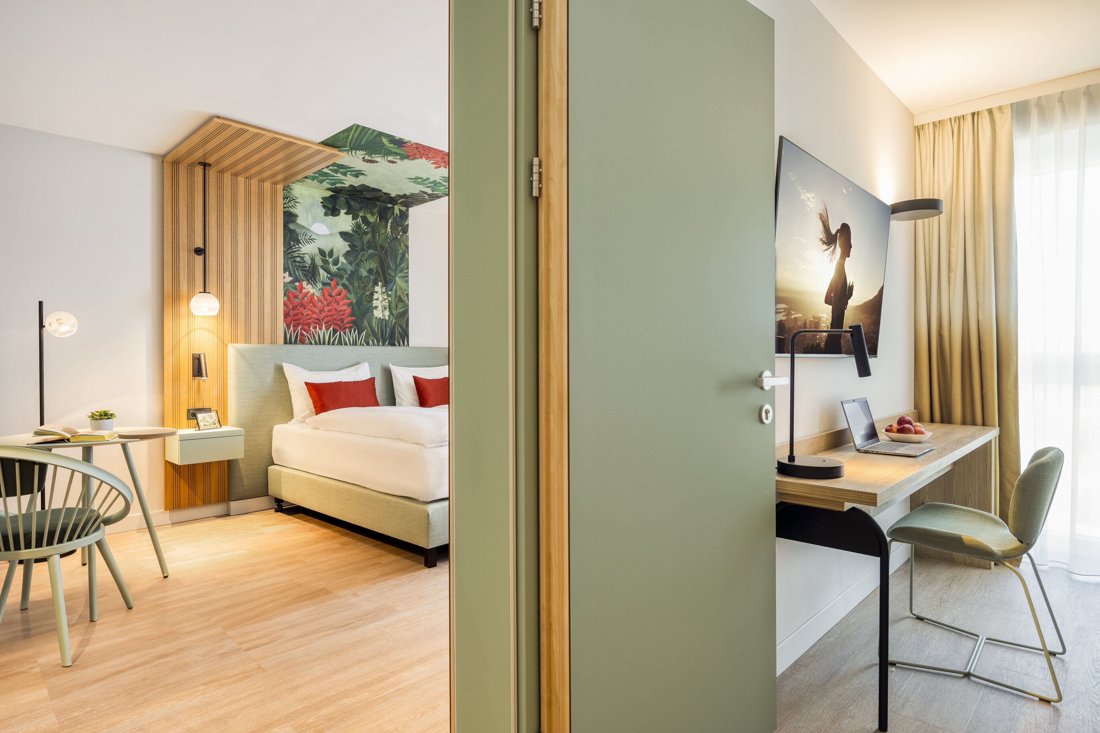 A hotel room with a bed, a desk, a chair, a small table, a lamp, and a painting on the wall.