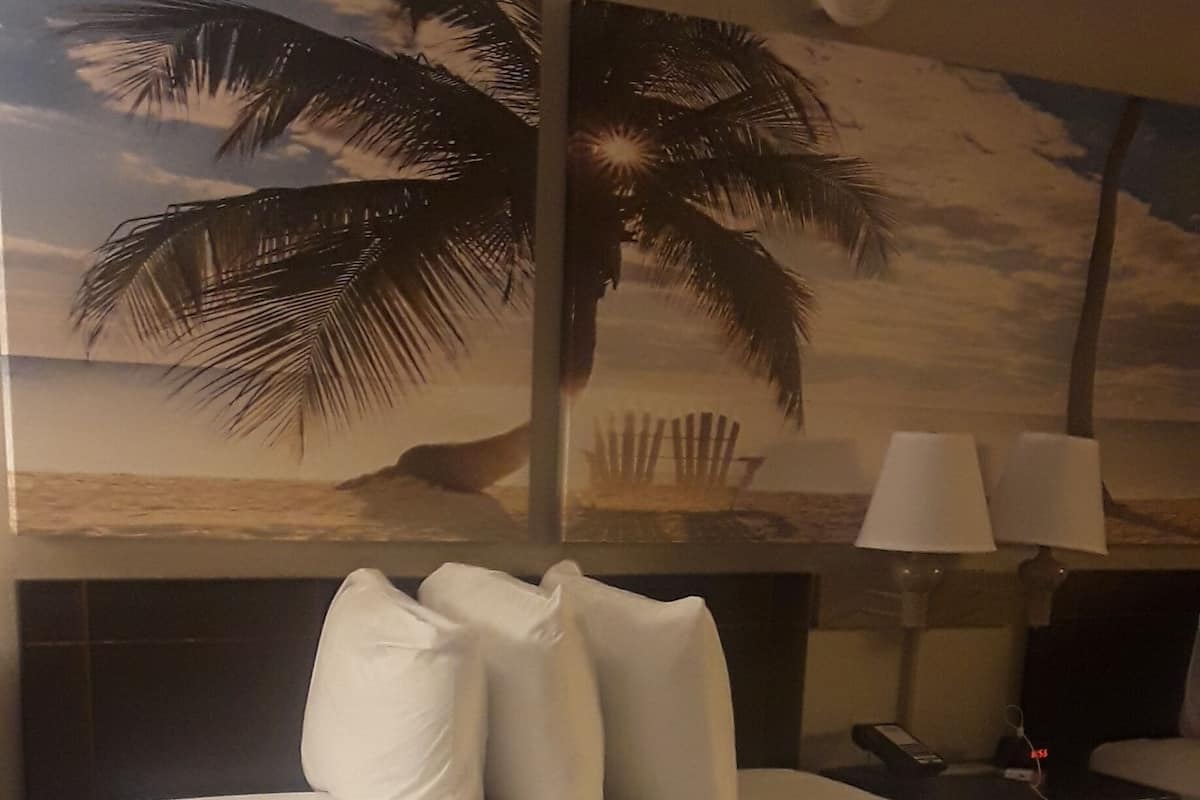 A hotel room with a large bed, a nightstand, a lamp, and a wall mural of a beach scene.