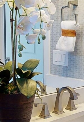 Un baño con una orquídea en maceta, un perchero con una toalla blanca y un grifo moderno.
