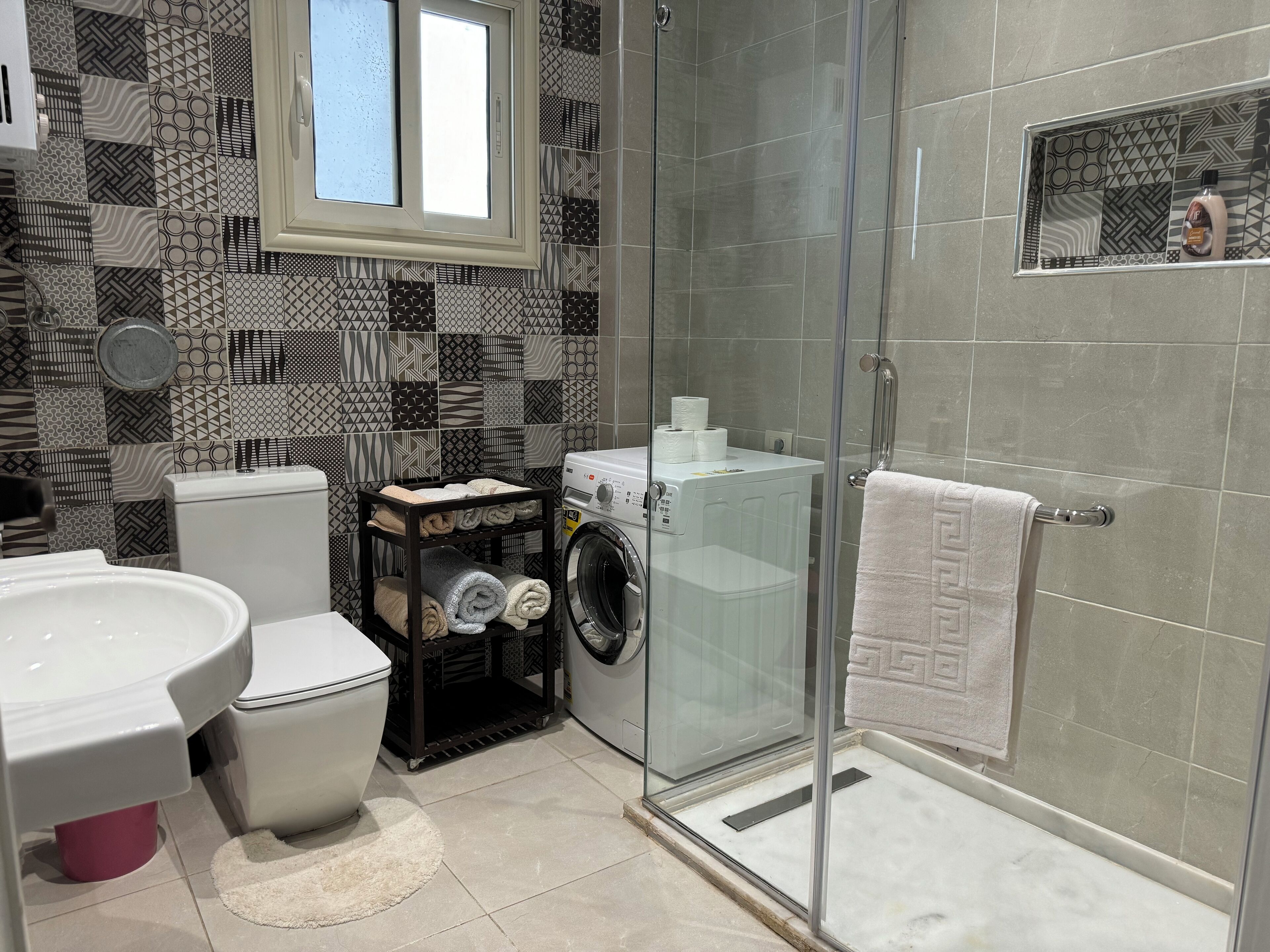 A modern bathroom with a glass-enclosed shower, a toilet, a washing machine, and a sink.