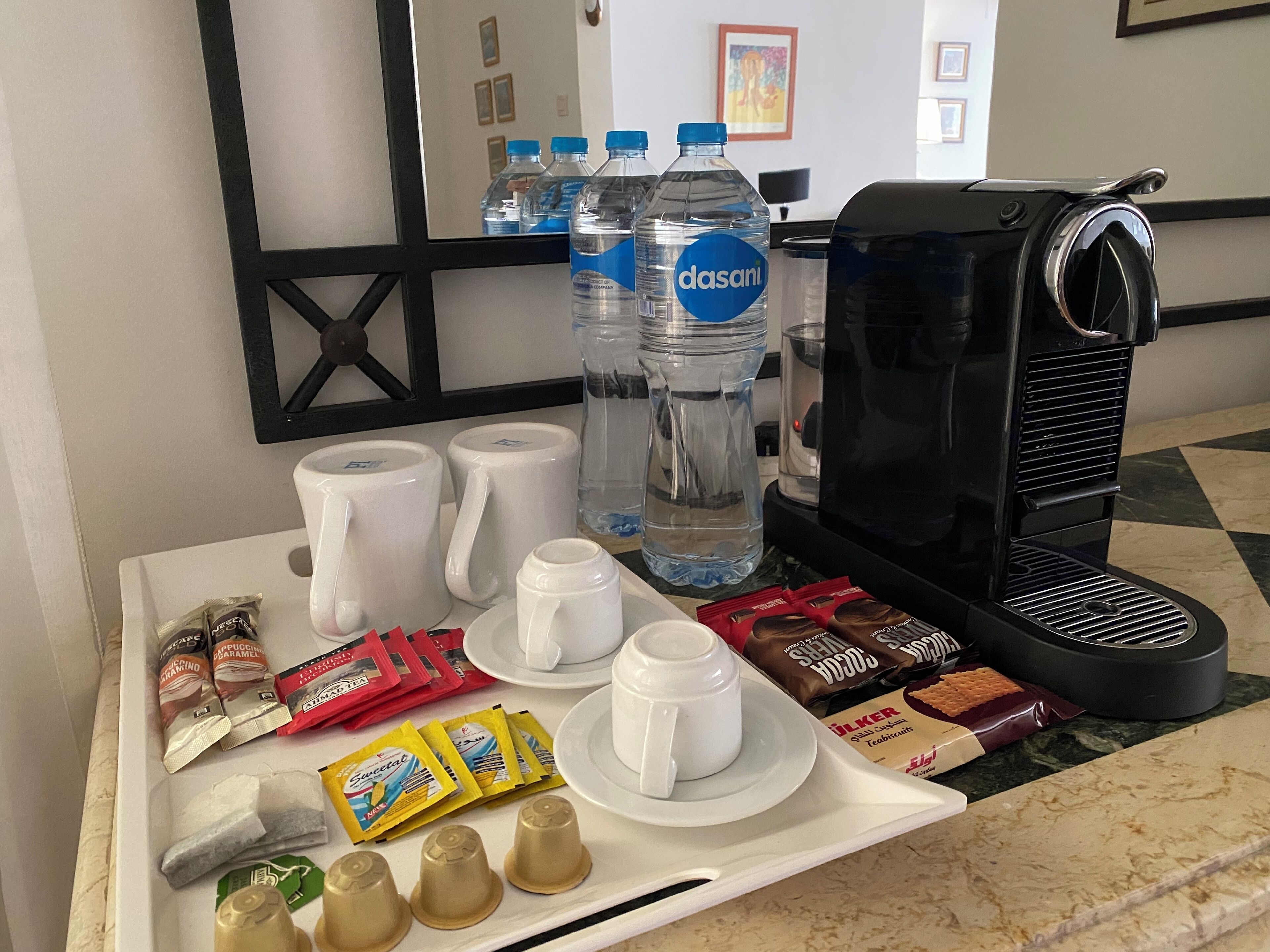 A breakfast tray with coffee maker, water bottles, coffee mugs, tea bags, and assorted snacks.