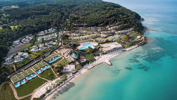 An aerial view of a coastal resort with multiple swimming pools, a beach, and a forested area.