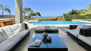 A poolside area with a view of the sea, outdoor seating, and a pergola.