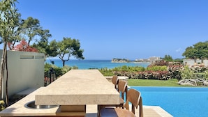 A poolside dining area with a view of the sea and a distant building.