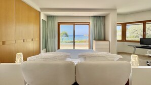 A hotel room with a bed, a desk, a TV, and a view of the sea.
