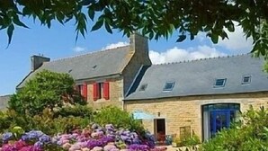 A traditional stone building with a blue door, surrounded by lush gardens with purple and pink flowers. - NEW: La Grange (Ploubezre)