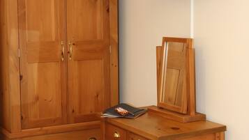 A room with a wooden wardrobe, a desk with a mirror, and a television displaying "THE WAVES".