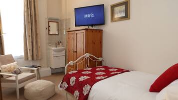 A bedroom with a bed, a TV, a wooden cabinet, a chair, and a small table.