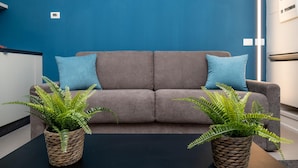A modern living room with a grey sofa, two blue cushions, and two potted ferns on a black table. - Imbriani Suites (Rome)