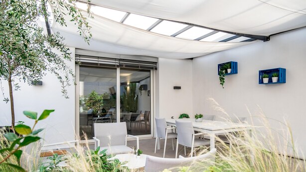 An outdoor patio with a glass door leading to a dining area, surrounded by greenery and white furniture. - Imbriani Suites (Rome)