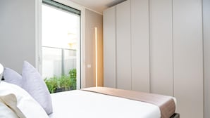 A bedroom with a bed, pillows, a bedside table, and a window with a view of greenery outside. - Imbriani Suites (Rome)