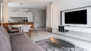 A modern living room with a flat-screen TV, a sofa, a dining area with chairs, and a kitchen in the background. - Imbriani Suites (Rome)