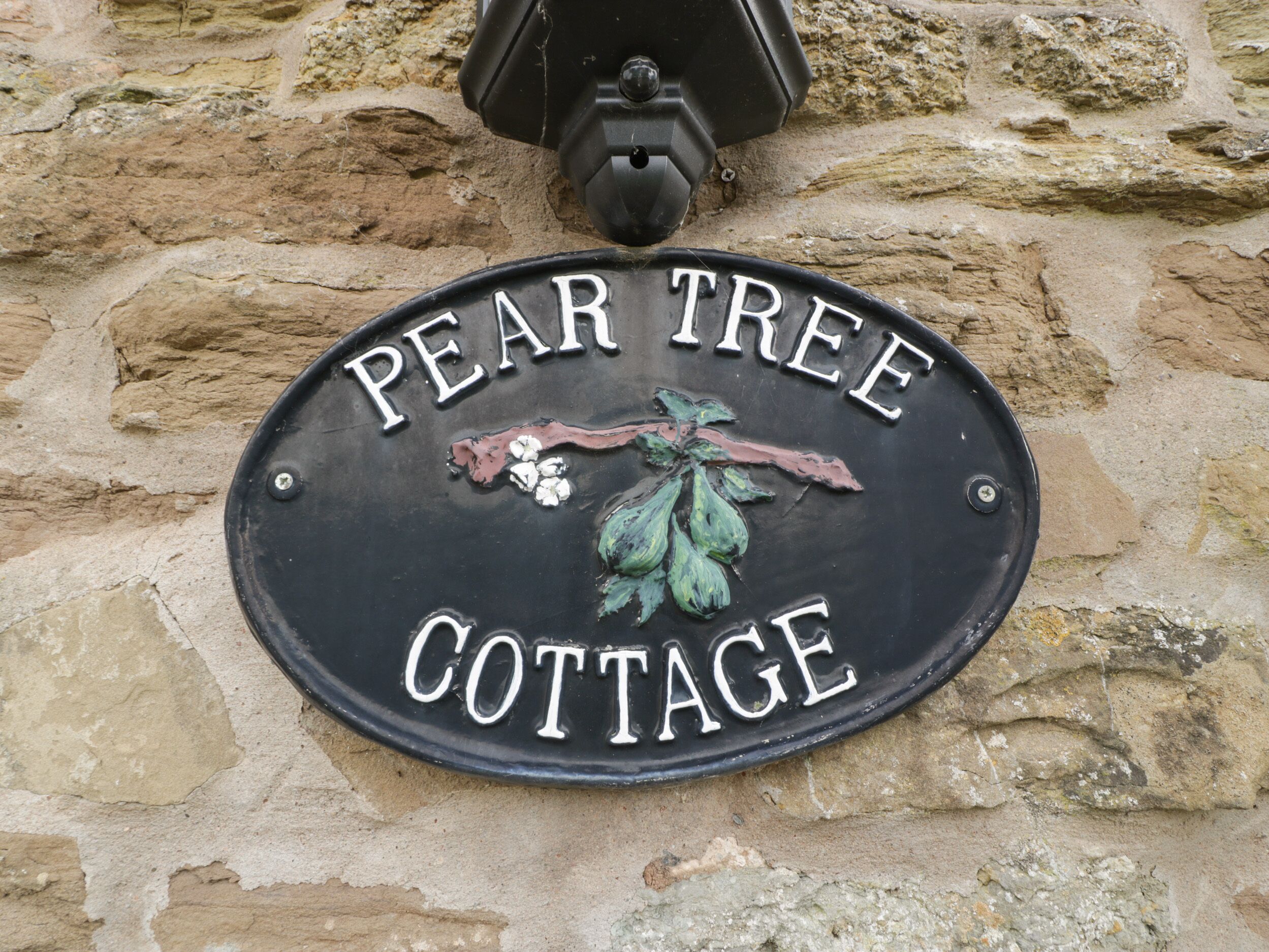 Ein schwarzes Metallschild mit der Aufschrift "PEAR TREE COTTAGE" und einem dekorativen Blattmuster.