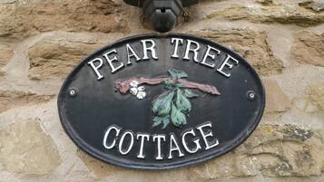 Ein schwarzes Metallschild mit der Aufschrift "PEAR TREE COTTAGE" und einem dekorativen Blattmuster.