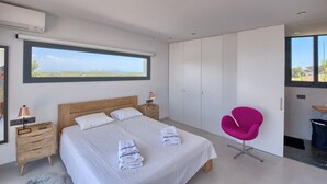 A modern bedroom with a large bed, a bright window, a wardrobe, and a unique pink chair. - Villa 'Amapola' with Mountain View, Wi-Fi and Air Conditioning (Begur)