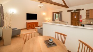 Un comedor con mesa de madera, sillas, televisor y zona de cocina con armarios y ventana.