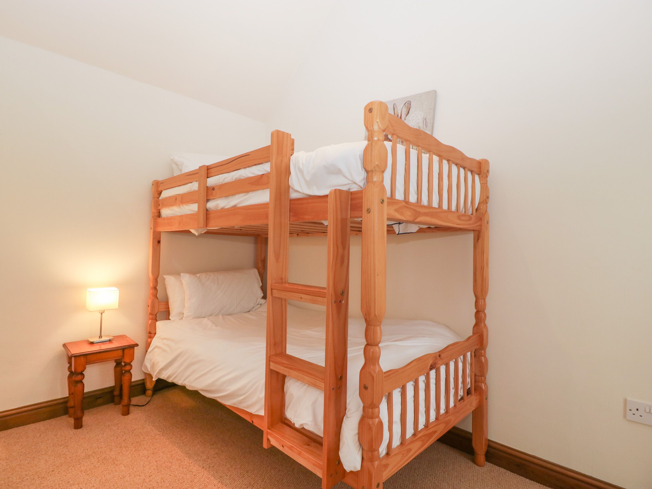 A bunk bed with a wooden frame, a bedside table with a lamp, and a wall-mounted artwork.
