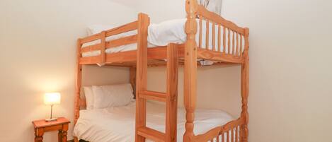 A bunk bed with a wooden frame, a bedside table with a lamp, and a wall-mounted artwork.