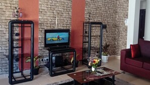 A living room with a brick wall, a television, a red sofa, and a coffee table. - Impeccable 3-bed Apartment in Mombasa (Mombasa)