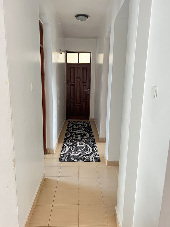 A hallway with a patterned rug, a wooden door, and a ceiling light.
