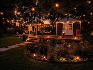 A house with a porch, a small shed, and a garden with flowers and a butterfly sculpture. - Burke Trammel Cottage • Pet-Friendly (Bonham)