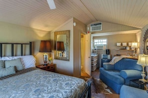 A bedroom with a bed, bedside table, lamp, and a large mirror. - Burke Trammel Cottage • Pet-Friendly (Bonham)