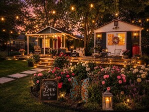 A cozy outdoor seating area with string lights, a welcome sign, and a variety of flowers. - Burke Trammel Cottage • Pet-Friendly (Bonham)