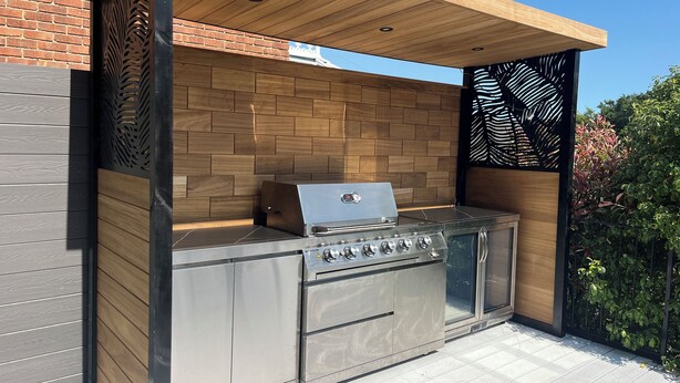 Ett modernt utomhuskök med en inbyggd grill, träpanel och en bakgrundsvägg av tegel.