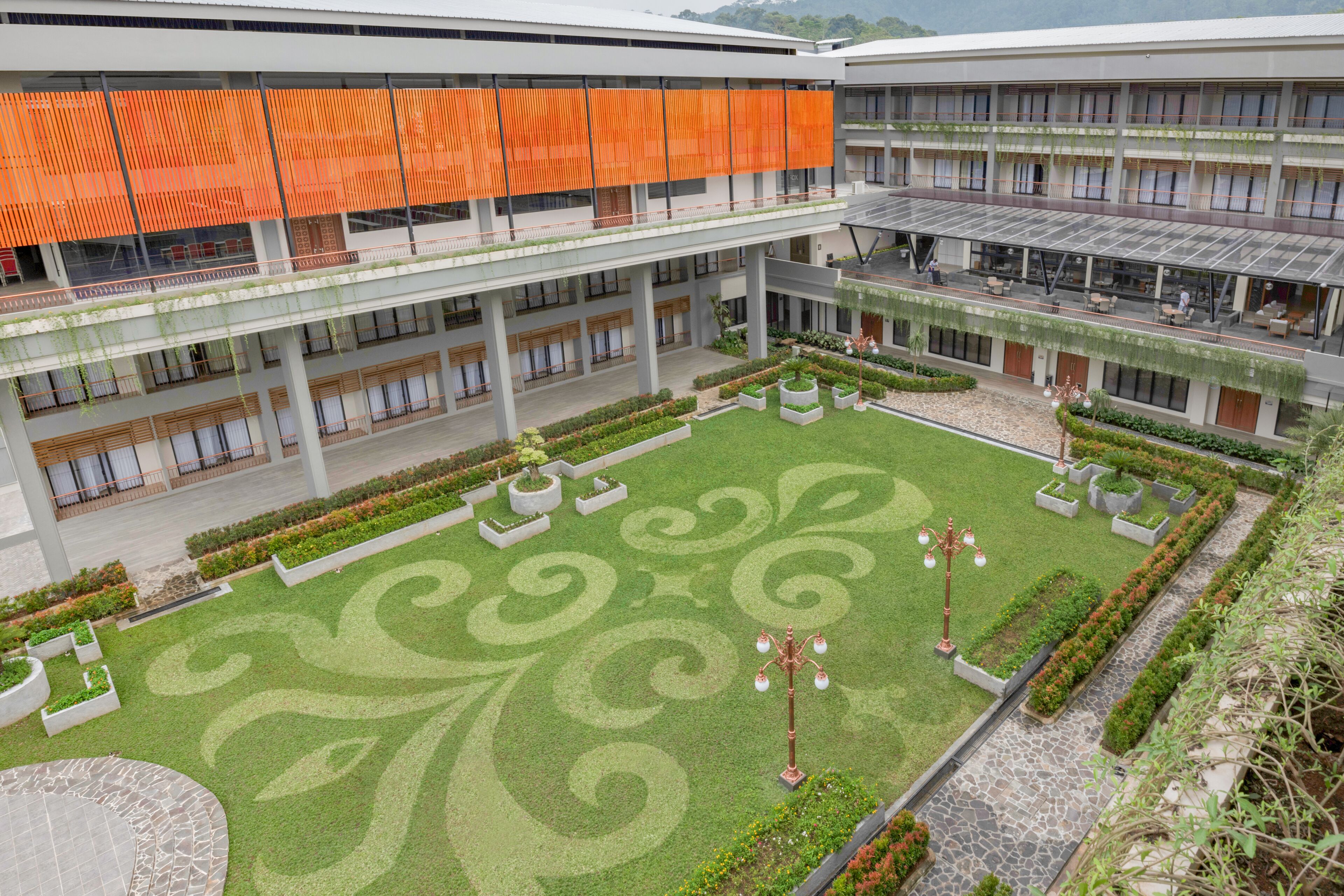 A modern building with a courtyard featuring ornamental grass patterns, planters, and a central light fixture.