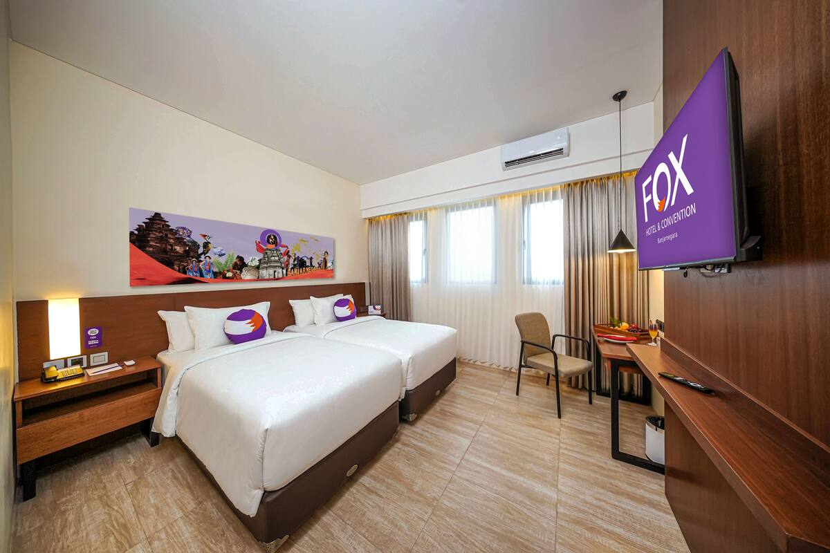 Ein Hotelzimmer mit zwei Betten, einem Schreibtisch, einem Sessel, einem Fernseher und einem Bild an der Wand.