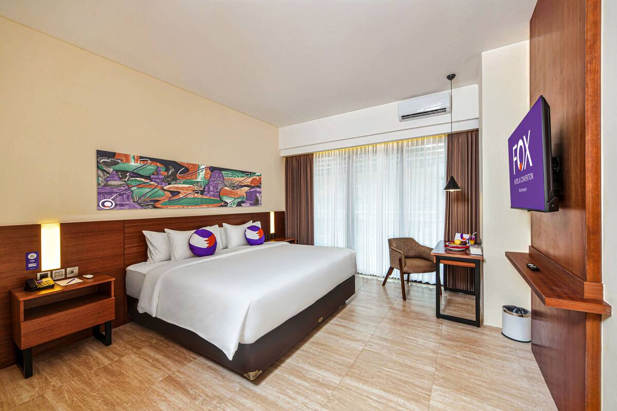 Ein Hotelzimmer mit einem großen Bett, einem Schreibtisch, einem Sessel, einem Fernseher und einem Bild an der Wand.