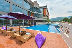 Uma área de piscina no terraço com espreguiçadeiras e guarda-sóis, piscina e um edifício moderno com grandes janelas.