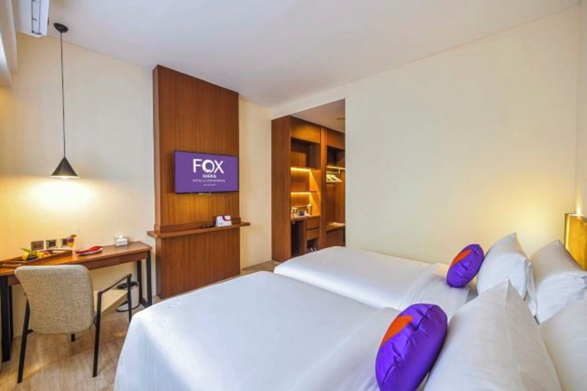 Une chambre d’hôtel avec deux lits, un bureau et un écran de télévision affichant le nom de l’hôtel.