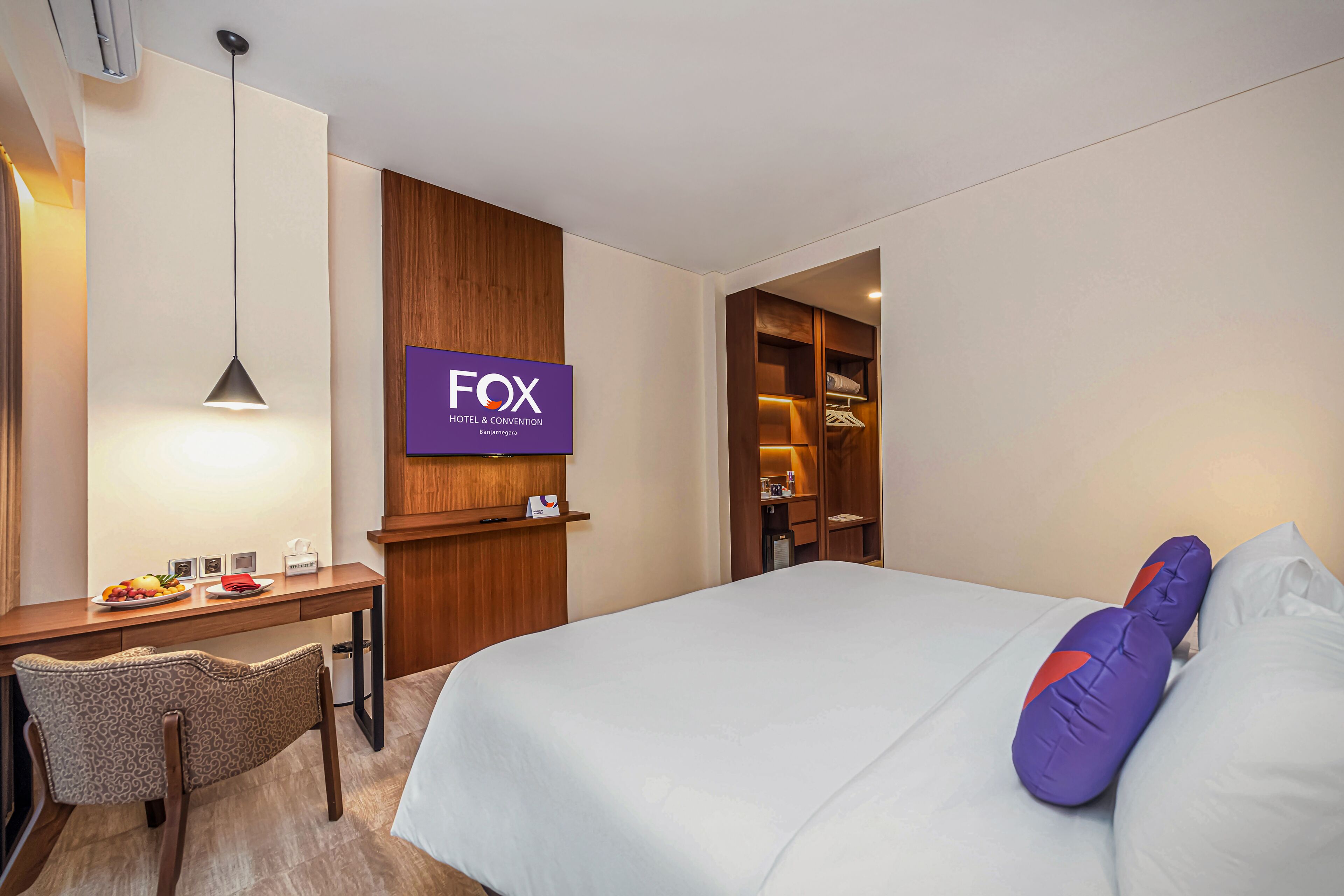 A hotel room with a bed, a desk, a chair, a TV, and a wardrobe.