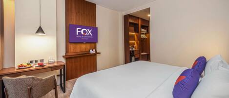 A hotel room with a bed, a desk, a chair, a TV, and a wardrobe.