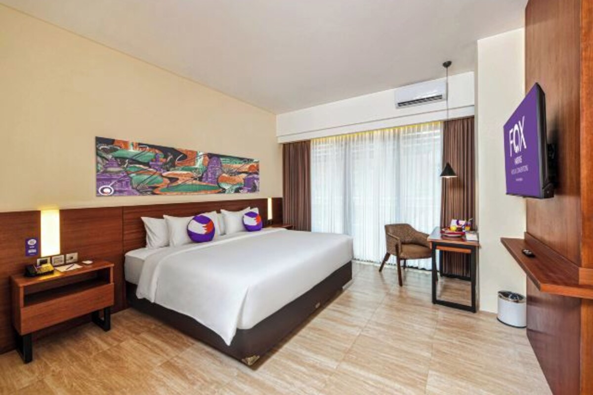 Une chambre d’hôtel avec un grand lit, un bureau avec une chaise, une télévision et un tableau au mur.